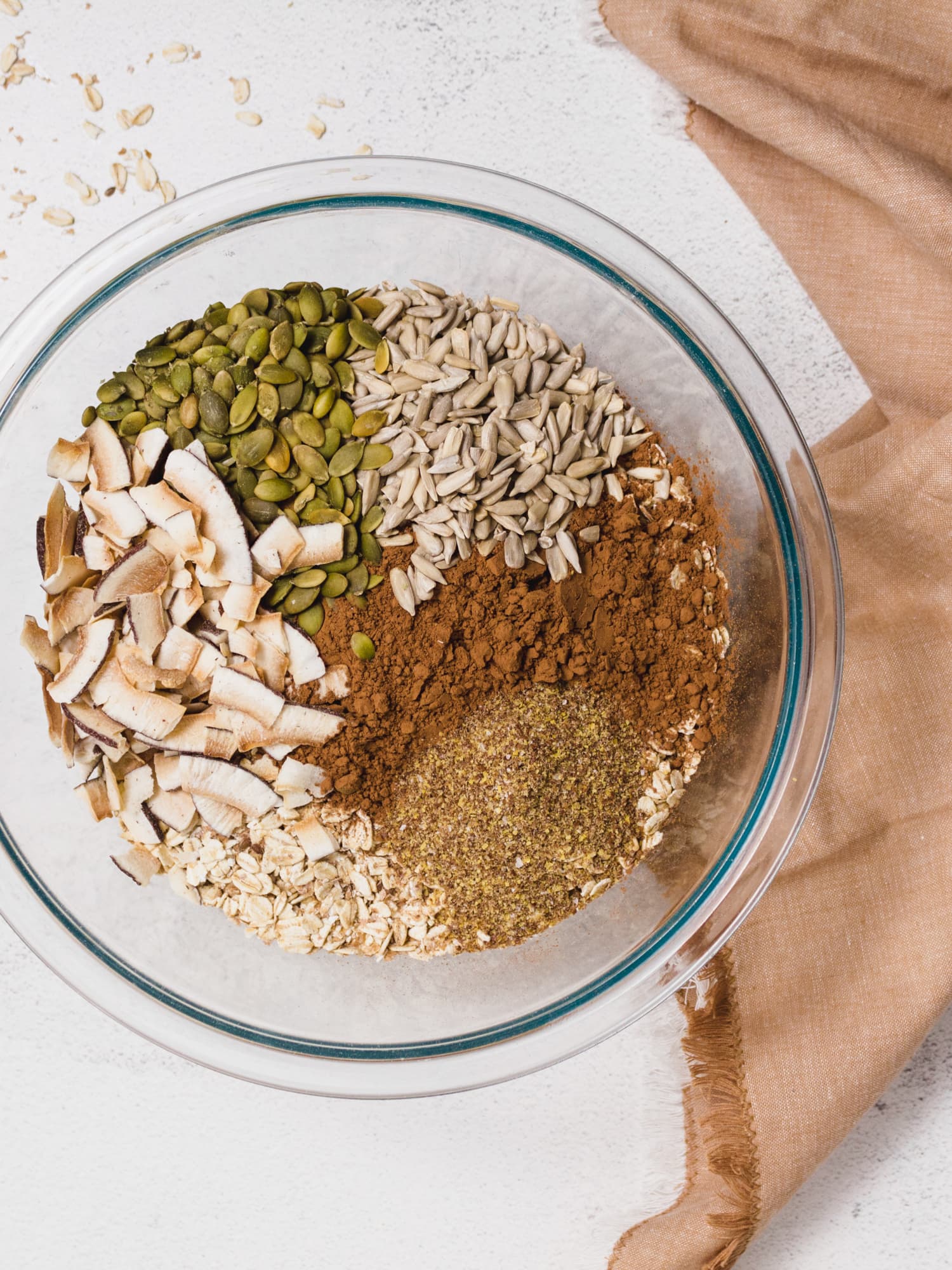 Dry ingredients in a bowl. Coconut smiles, pumpkin seeds, sunflower seeds, cocoa powder, ground flaxseed, and oats.  