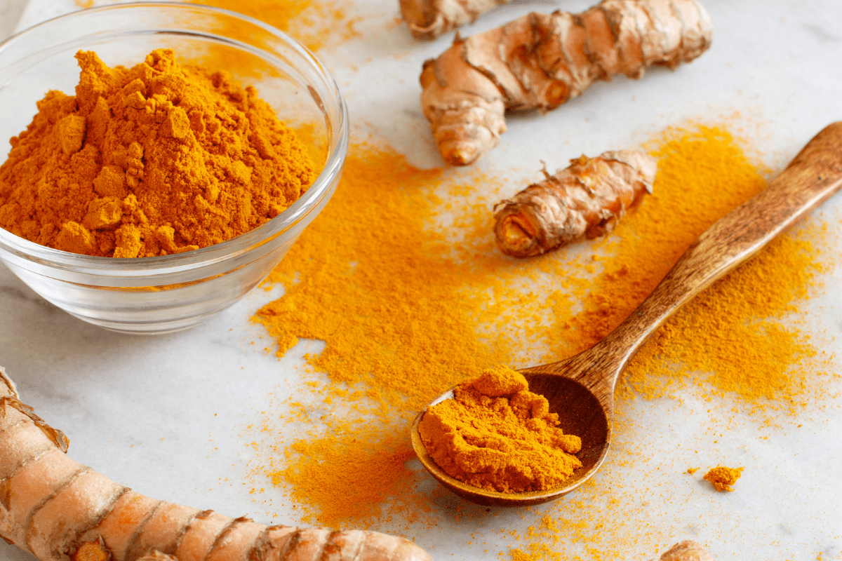 Turmeric powder on a white counter top in a wooden spoon. 