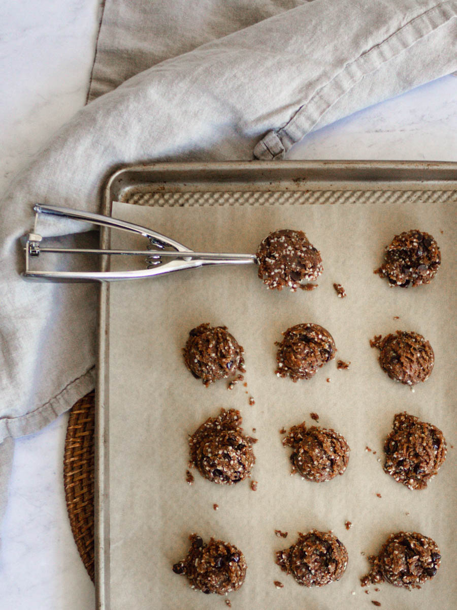 The cookies lined up on a baking sheet, before being baked. There is one left in the cookie scoop. 