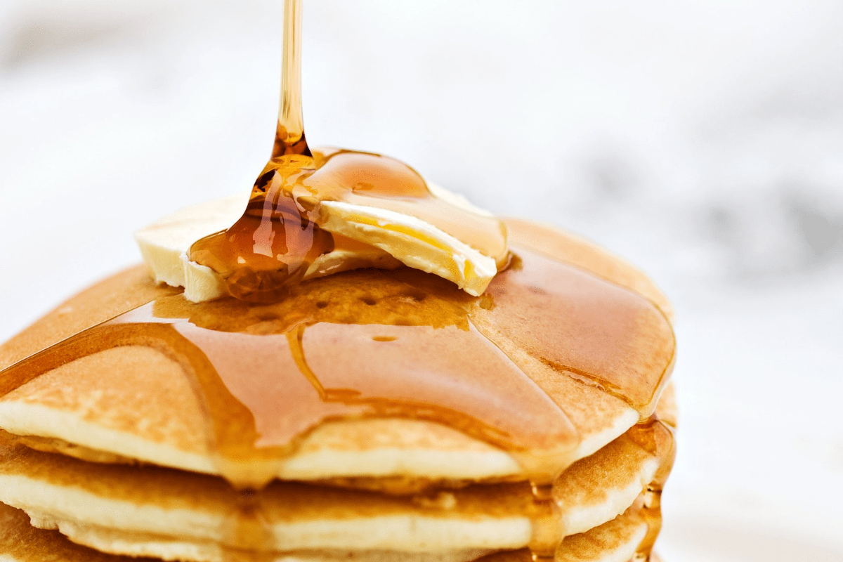 Stack of pancakes with syrup drizzling over top. 