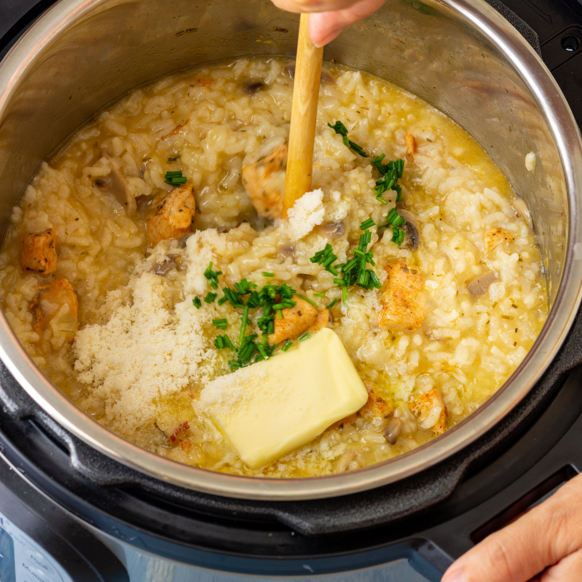 A hand stirring a rice dish being cooked in the pressure cooker. 