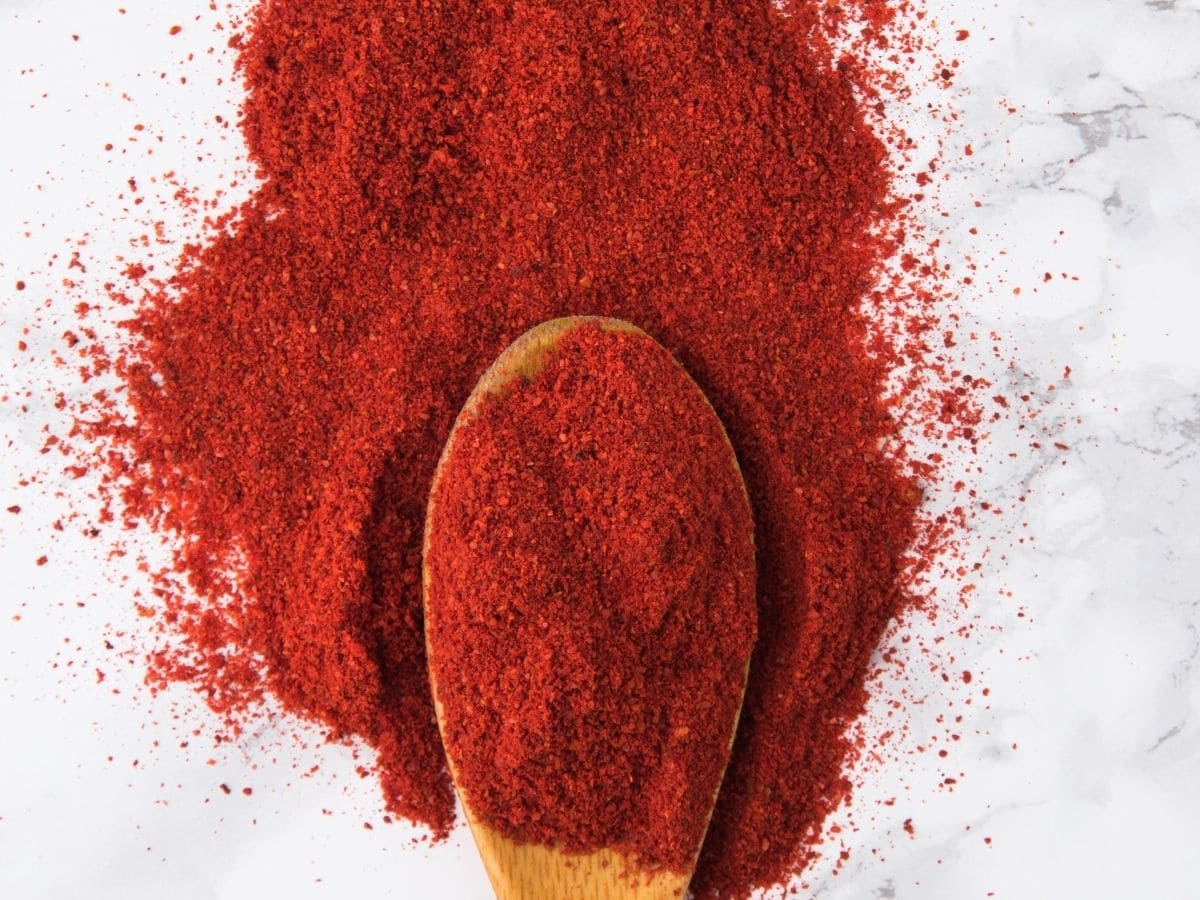 Smoked paprika in a wooden spoon on a white counter top. 