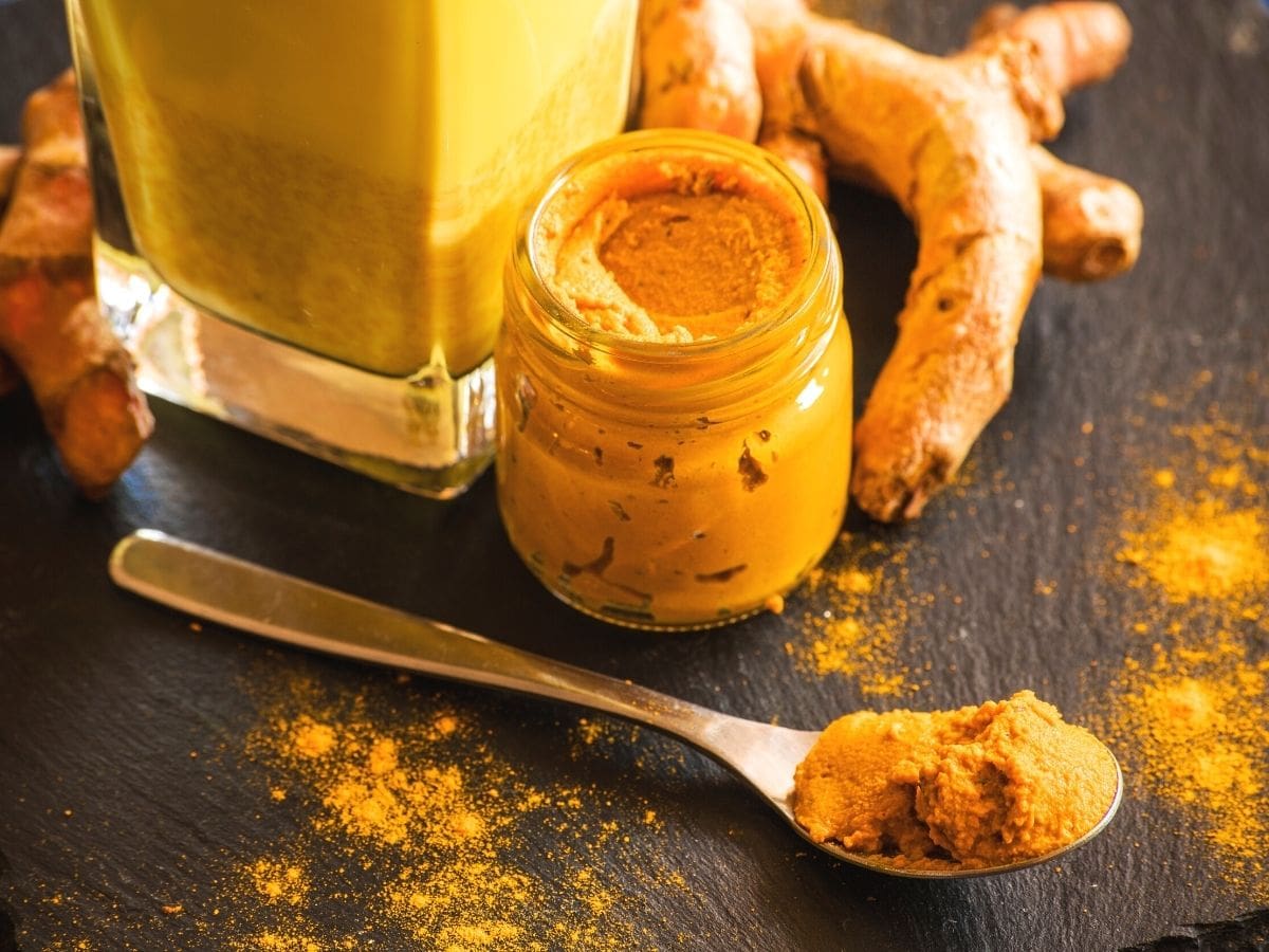 Turmeric paste in a glass jar. A spoonful of it sits on a wooden countertop. 