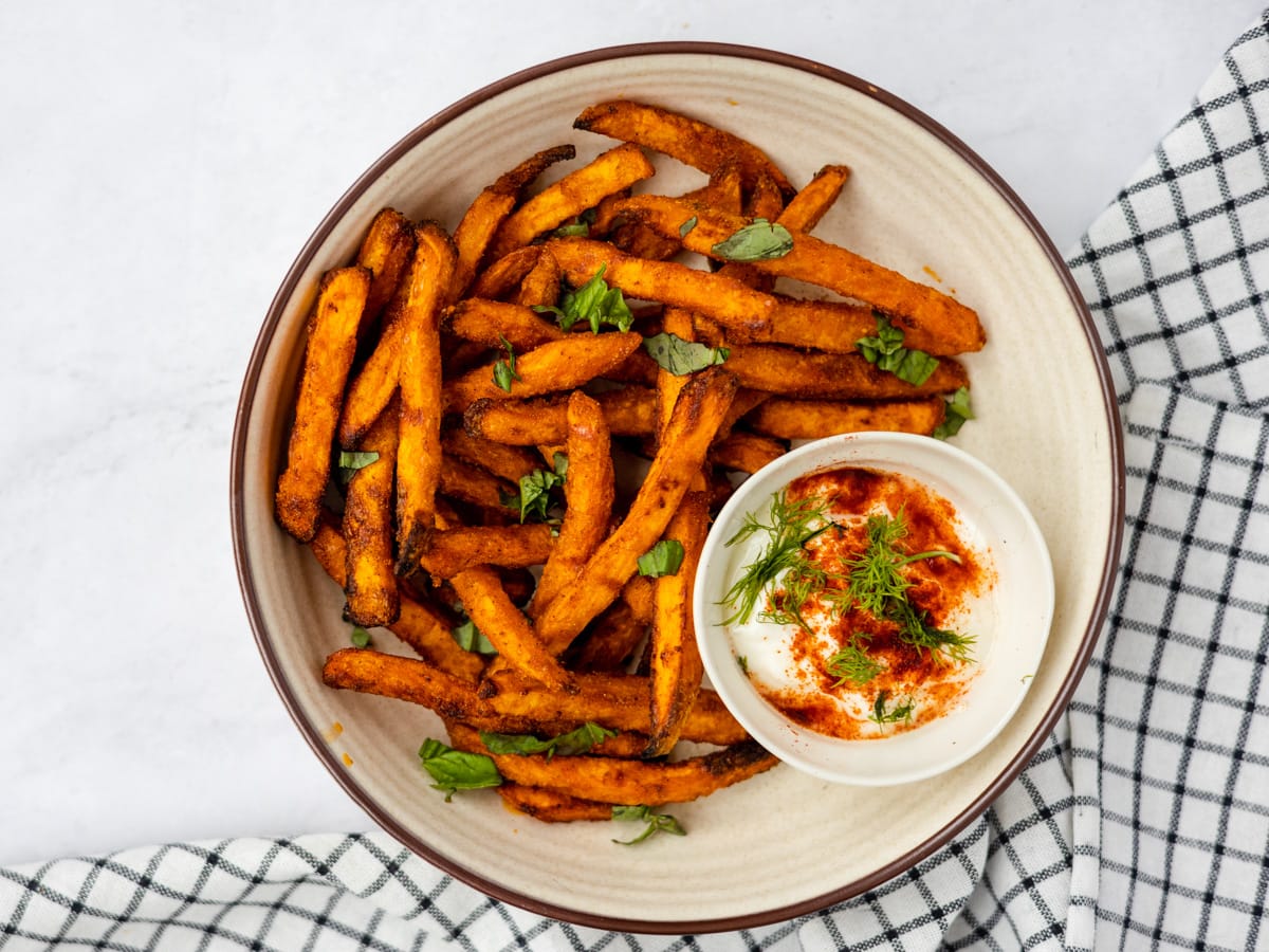 A bowl of sweet potato fries with a mayo dip and basil sprinkled on top.