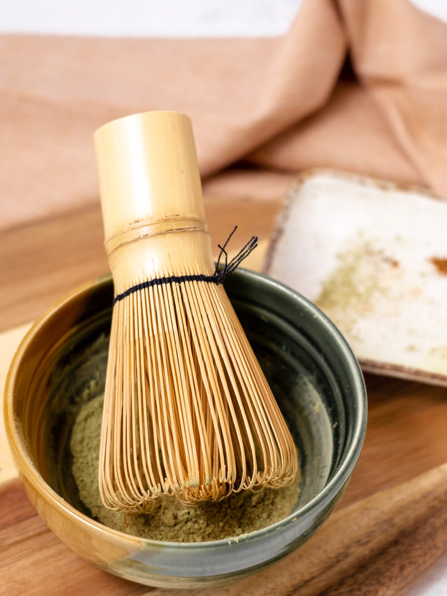Bamboo whisk in small green bowl with matcha powder. 