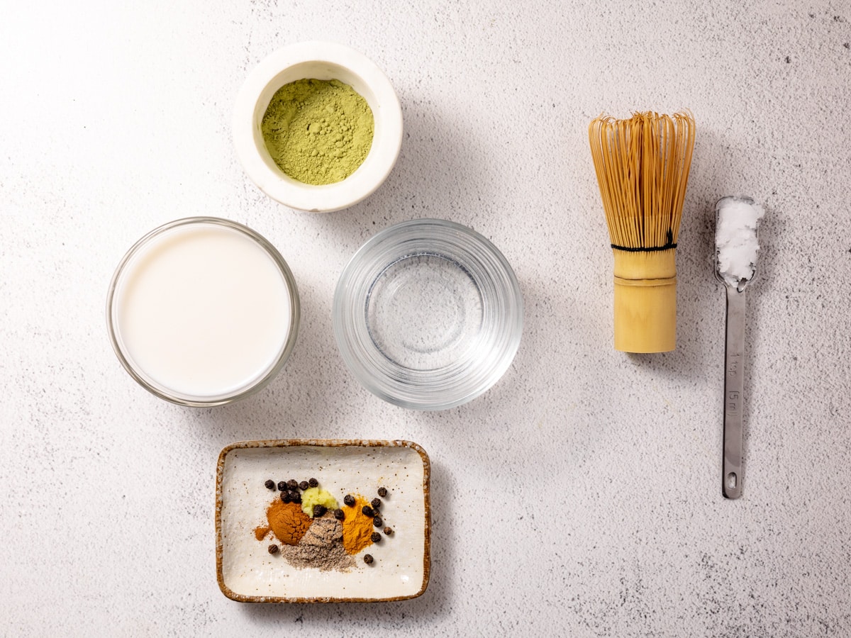 Ingredients needed to make a matcha turmeric latte. All are placed on a white countertop. 