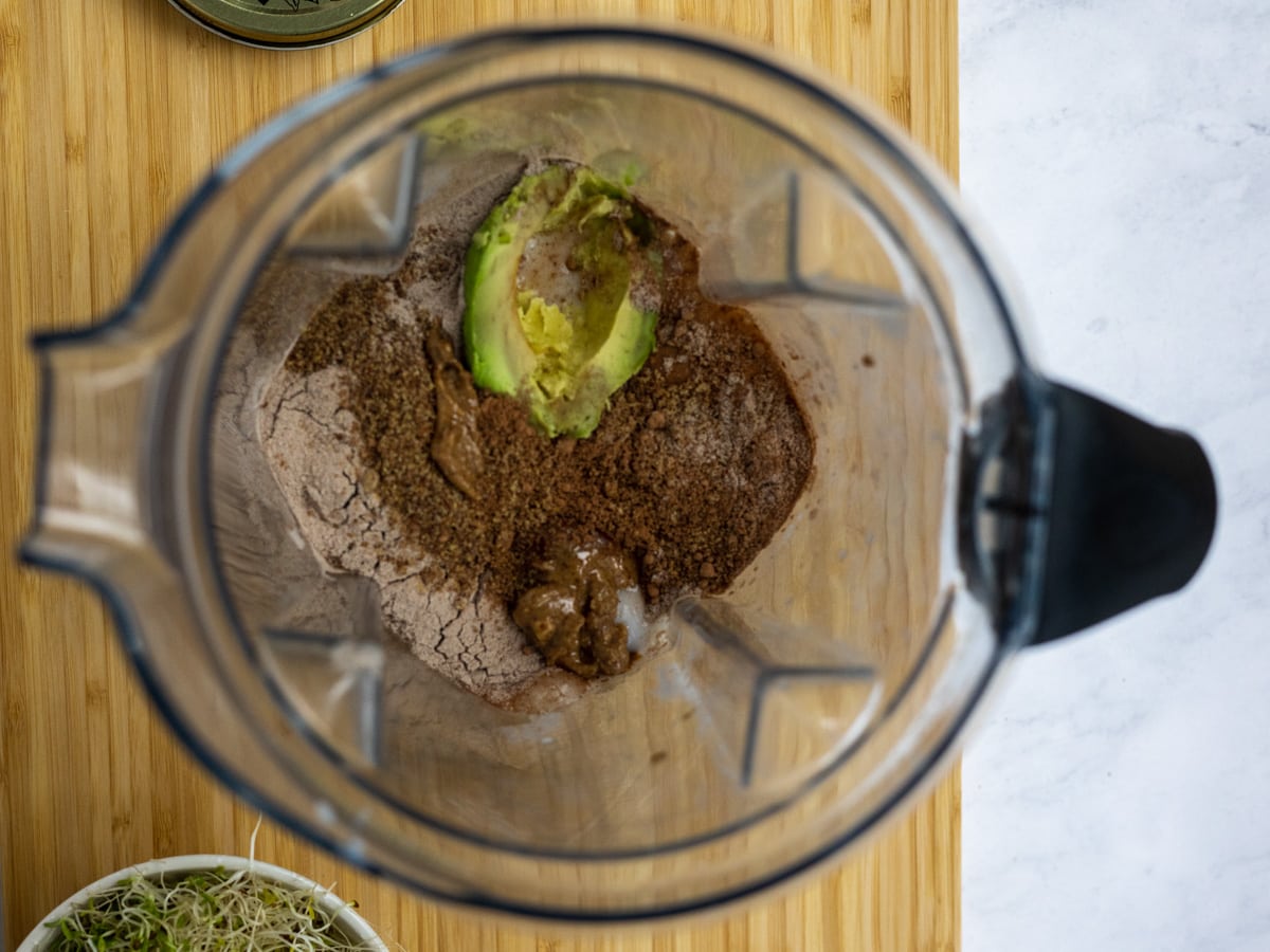 Ingredients inside a vitamix blender with an avocado just added on top. 