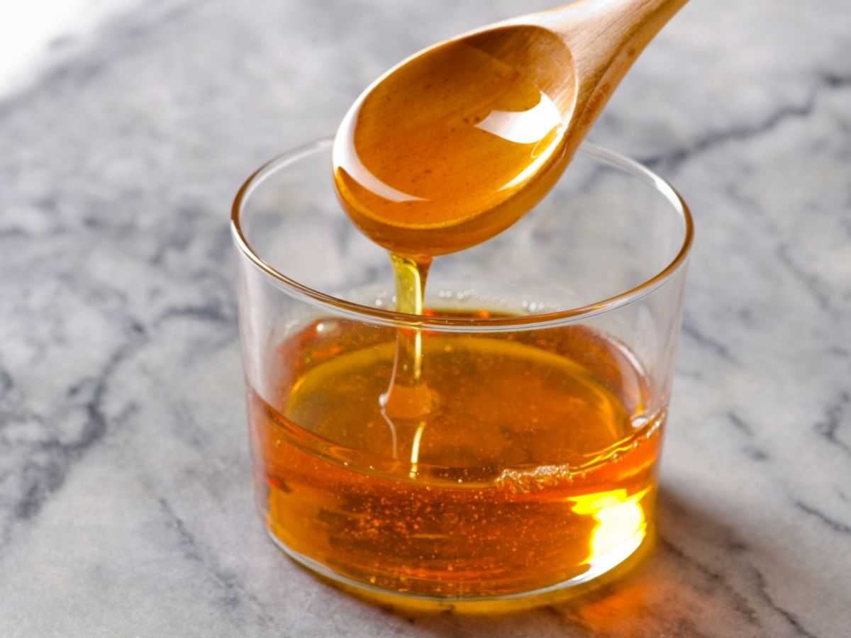 A spoonful of agave syrup dripping into a glass jar holding more agave syrup. 
