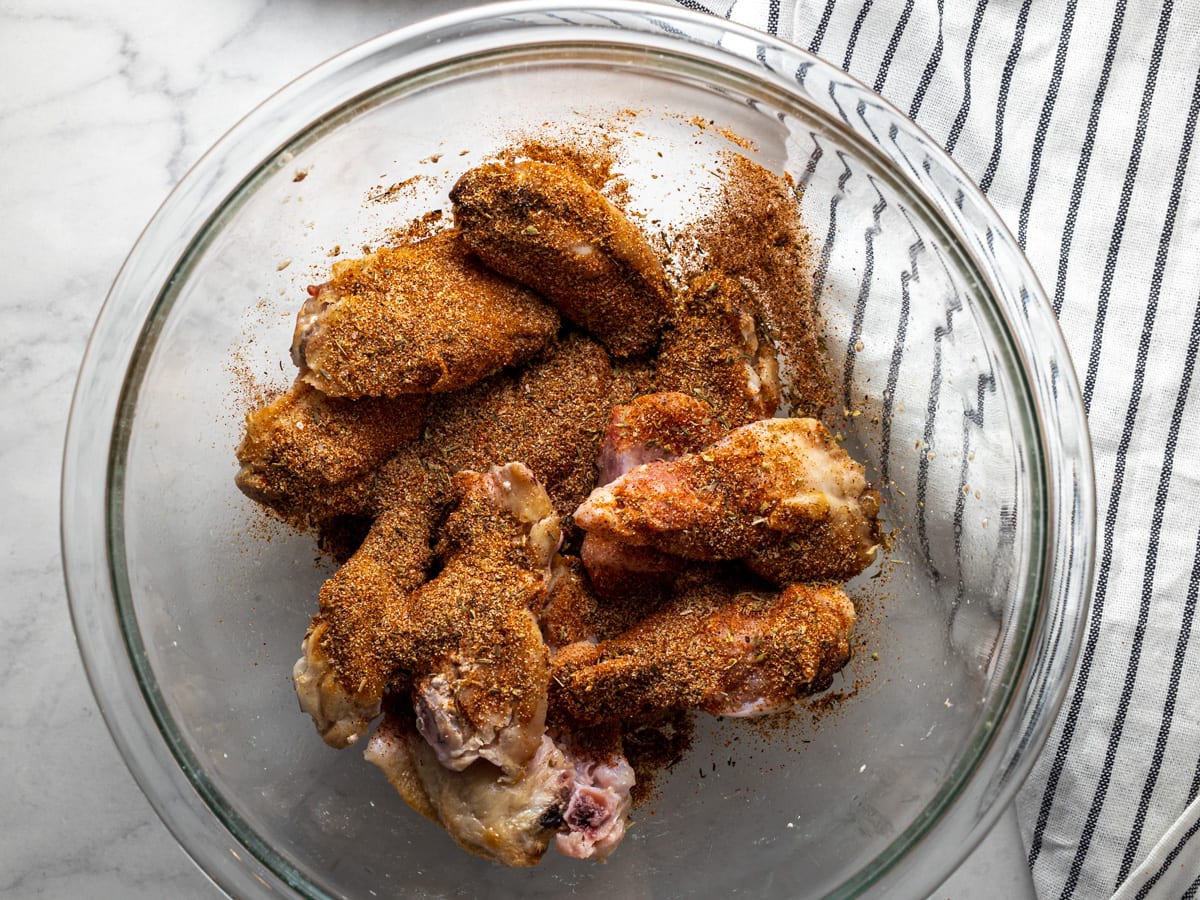 Frozen chicken wings in a glass bowl coated in a spice rub. 