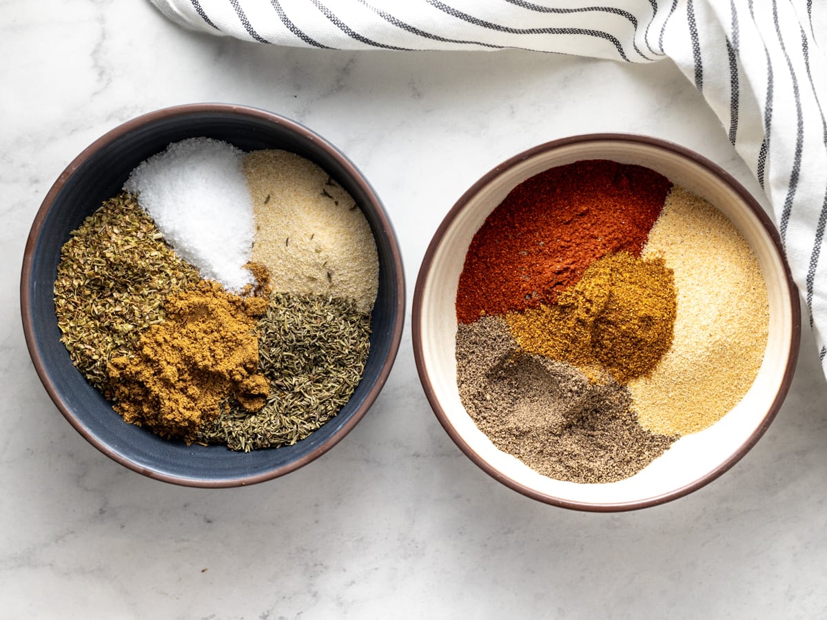 Spices needed to make chicken wing rub in two bowls on a marble countertop.