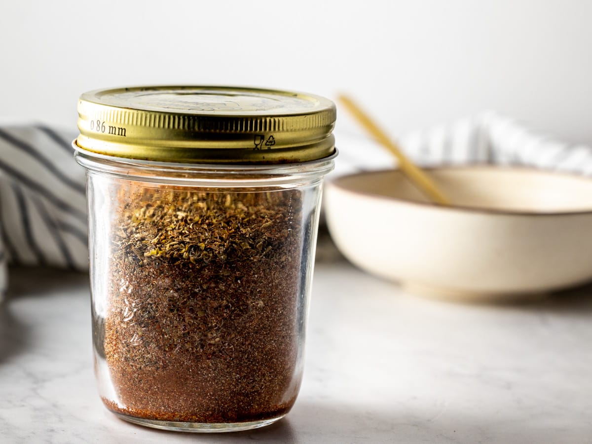 A mason jar filled with a spice rub. A bowl is in the background.