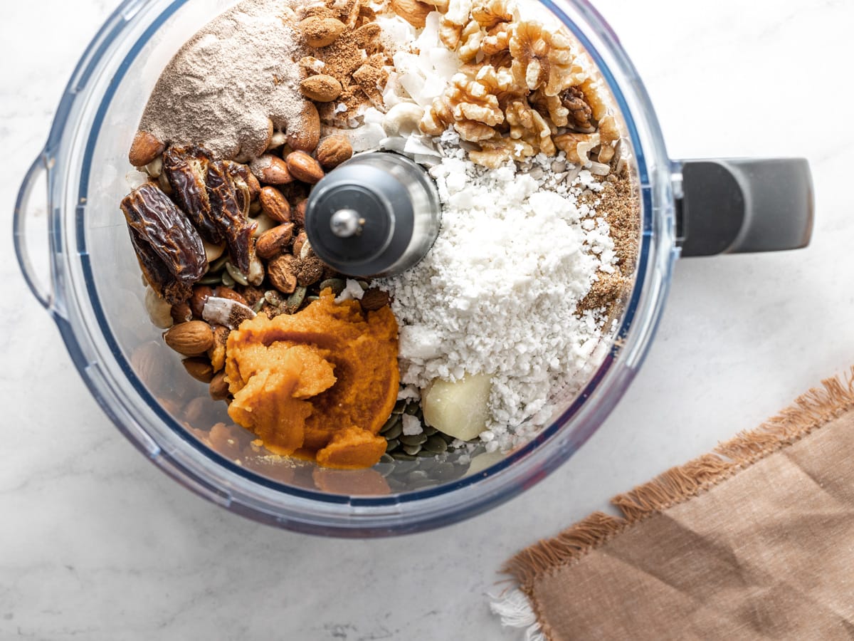 Ingredients needed to make pumpkin protein balls inside a food processor on a white countertop. 