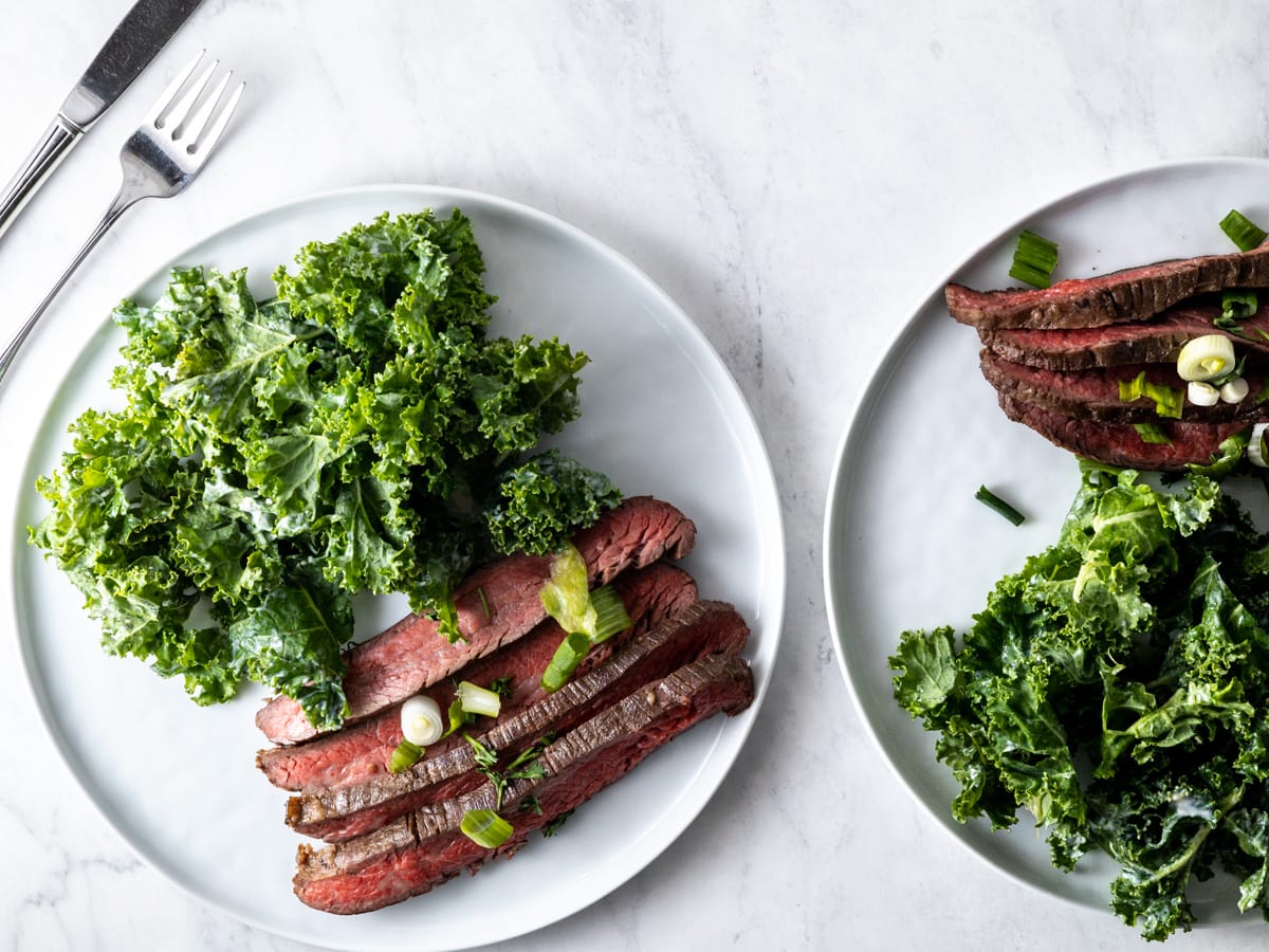 A flank steak and kale salad on a white plate. 