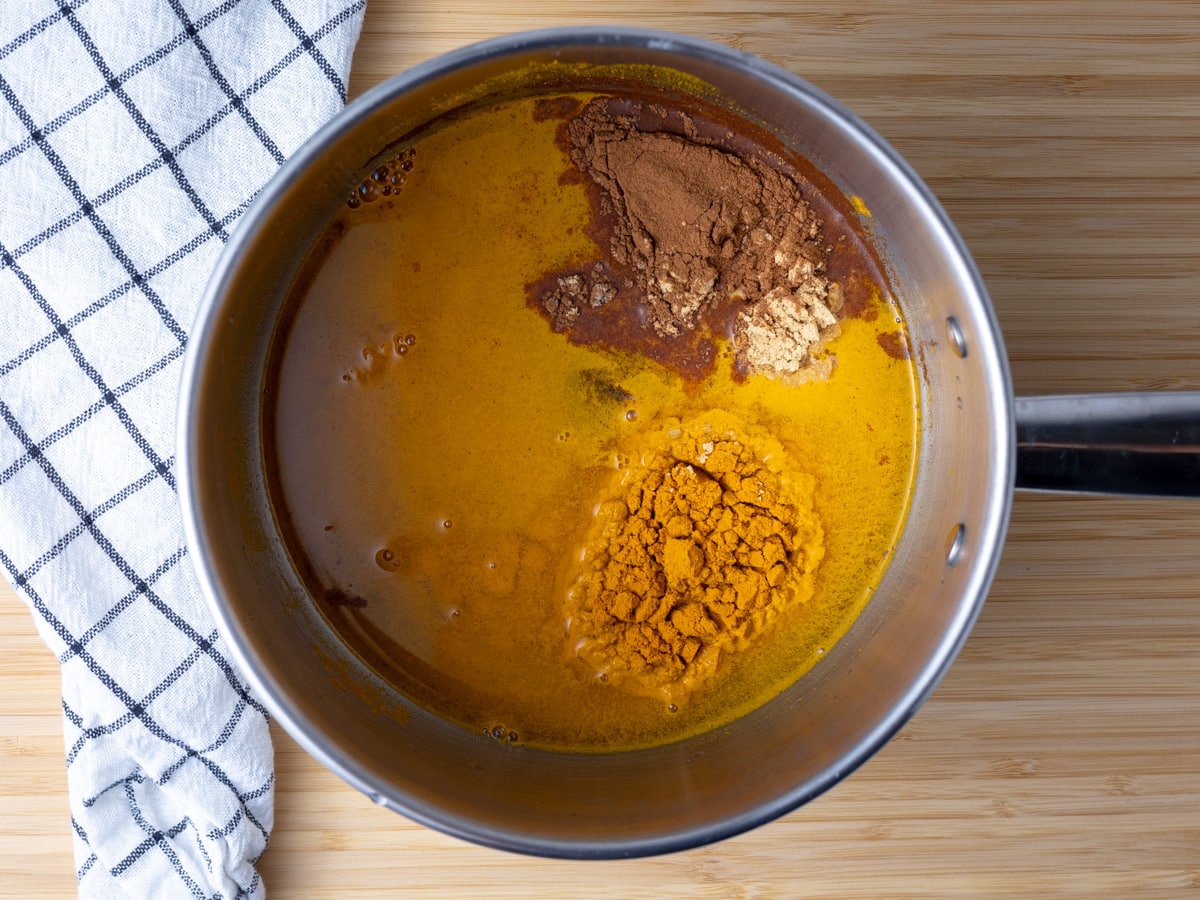 A small saucepan with turmeric, water, cinnamon, nutmeg, ginger, cardamom and turmeric in it. 