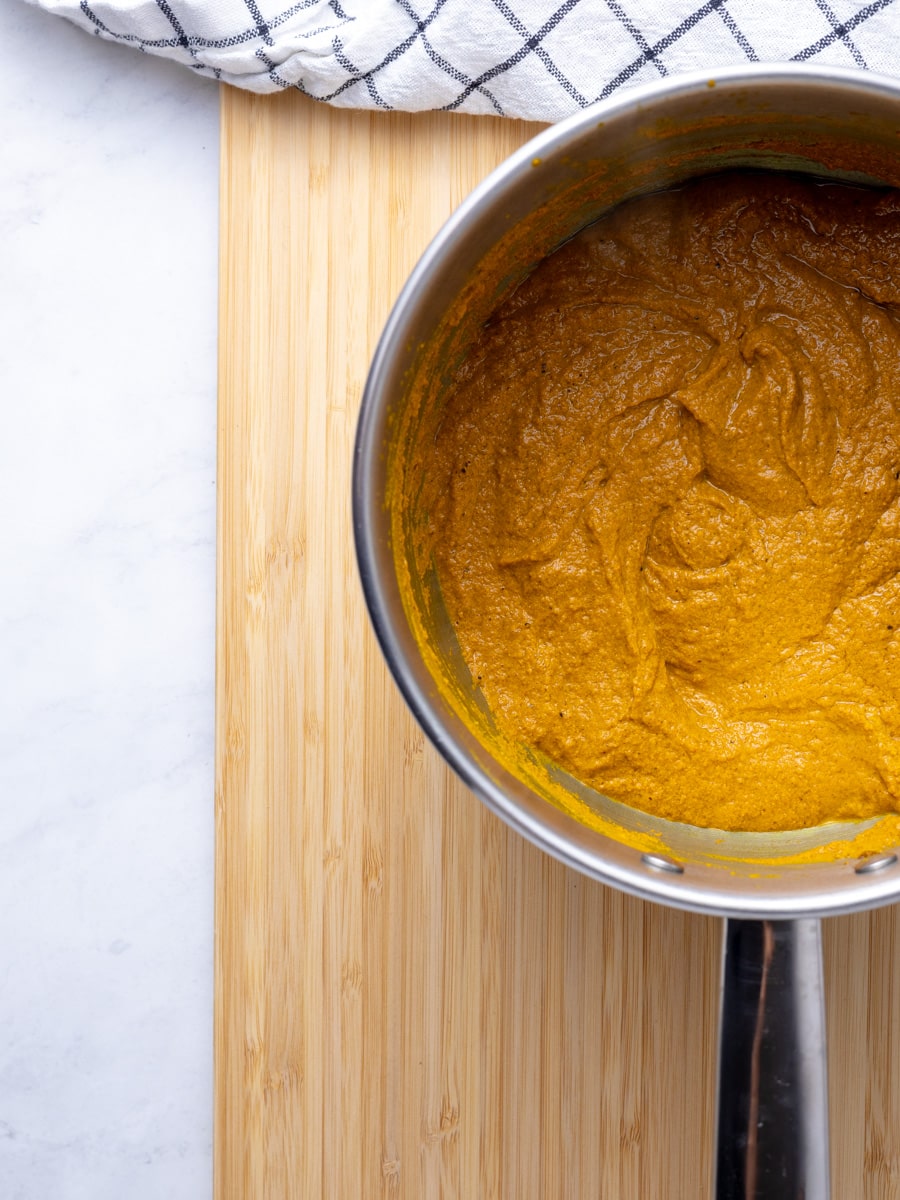 A small saucepan with a thickened turmeric paste in it. On a wooden cutting board. 