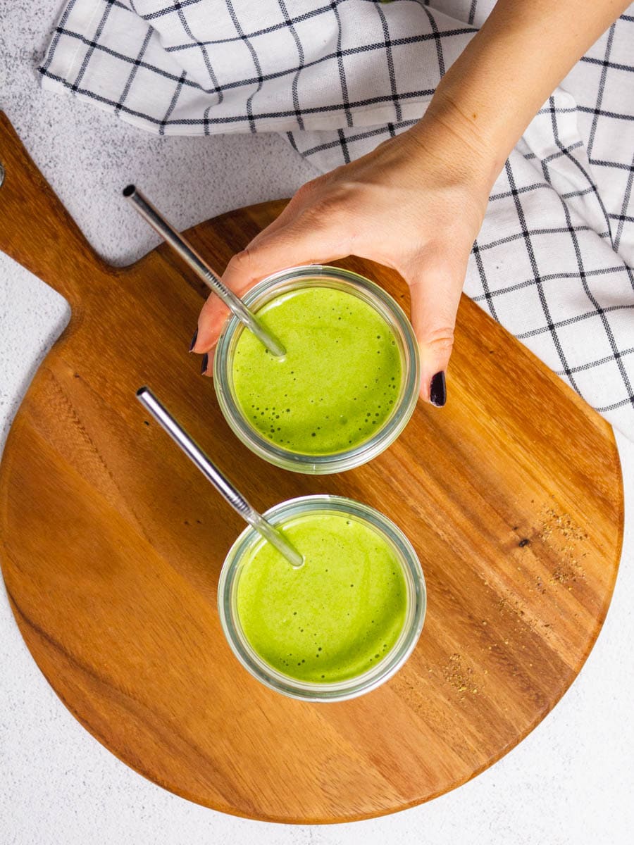 Two green smoothies on a wooden cutting board. 
