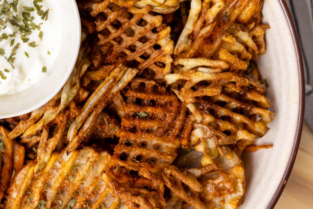 Up close shot of homemade waffle fries in a ceramic bowl.