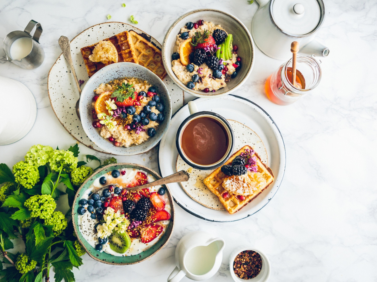 A breakfast spread with waffles, granola, yogurt and coffee on a white countertop. Shot from overhead.