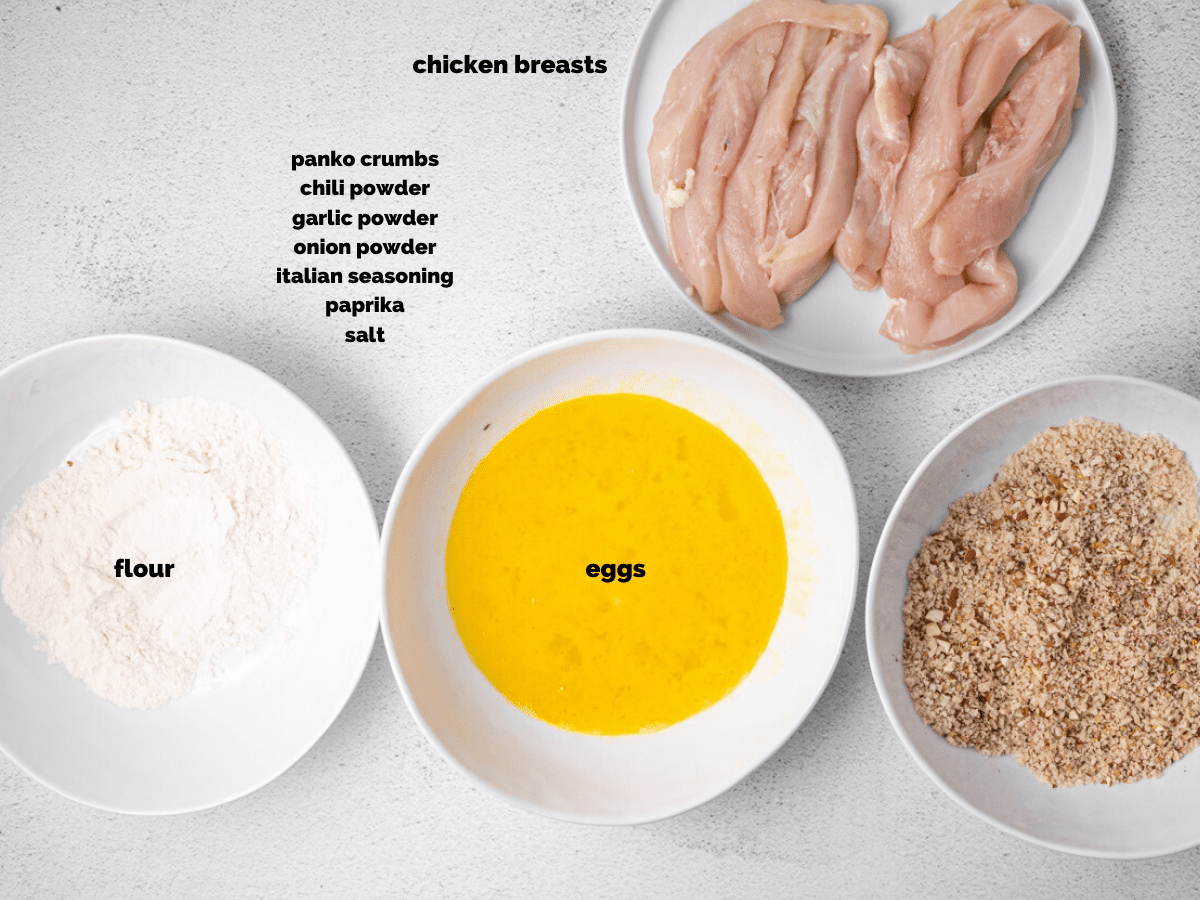 Ingredients needed to make air fryer chicken tenders. Layed out in bowls on a white countertop.