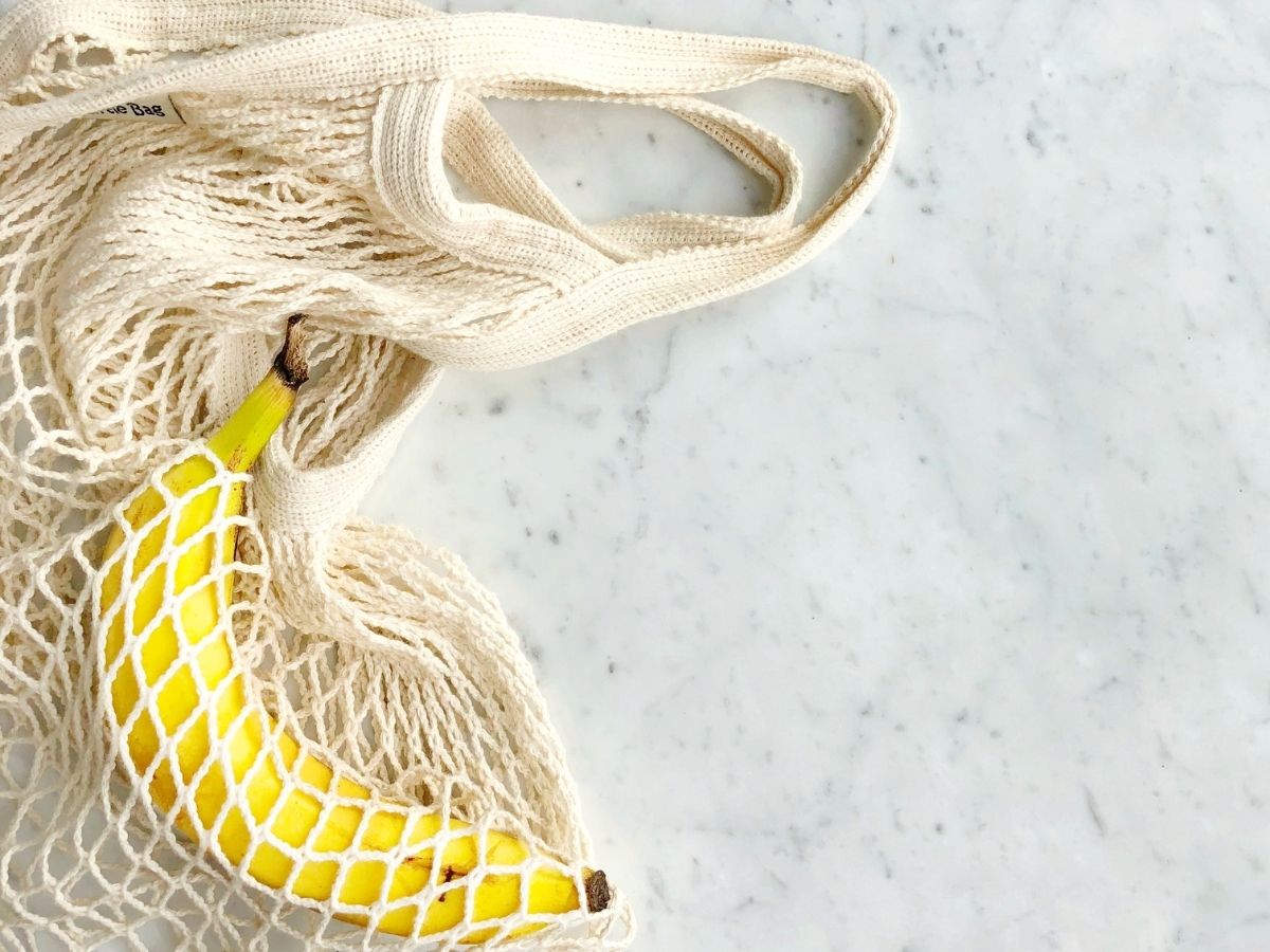 A banana in a mesh bag on a white countertop.