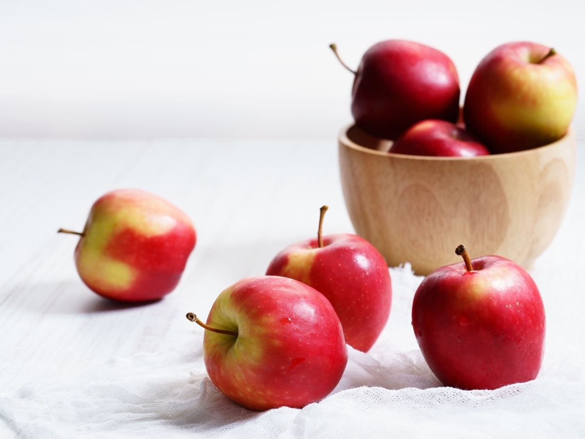 A wooden bowl filled with apples. Several apples have fallen out onto the countertop.