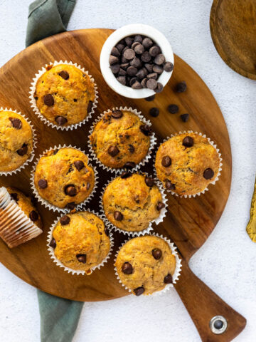 Banana chocolate chip protein muffins on a wooden cutting board with a gold vintage knife sitting nearby.