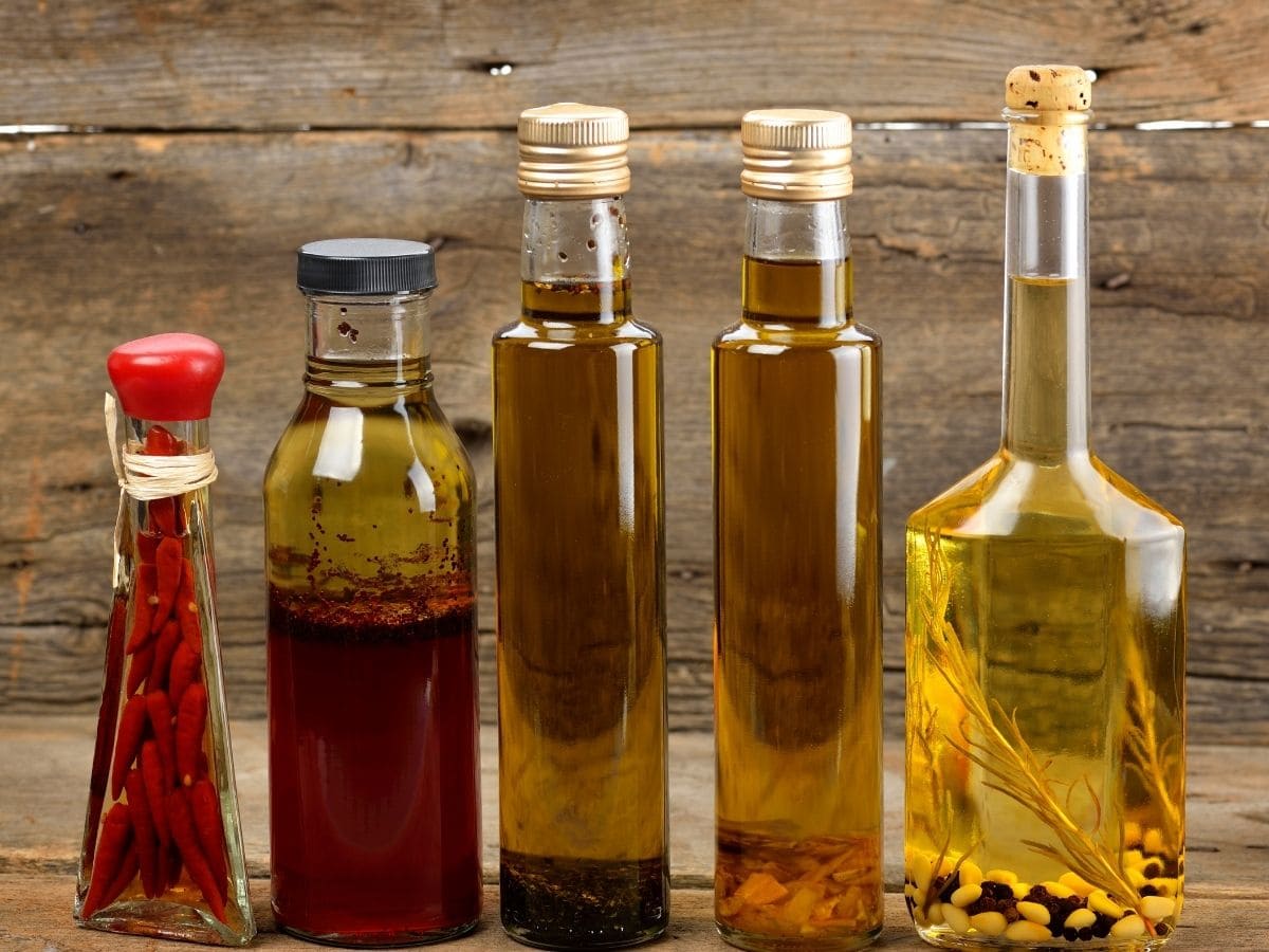 Five bottles of different kinds of oil in a row against a wooden backdrop.