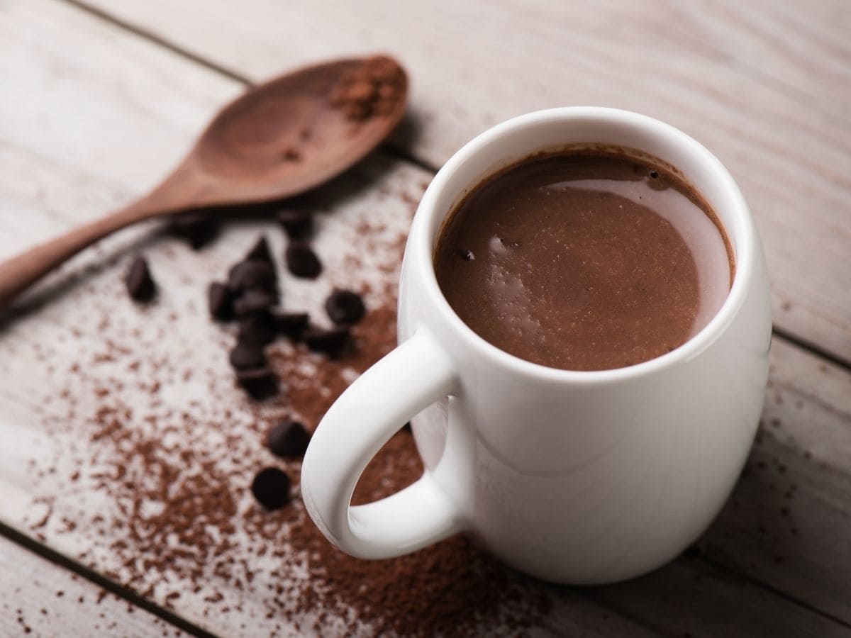 A cup of hot chocolate on a wooden background. Cocoa powder is spread around it.