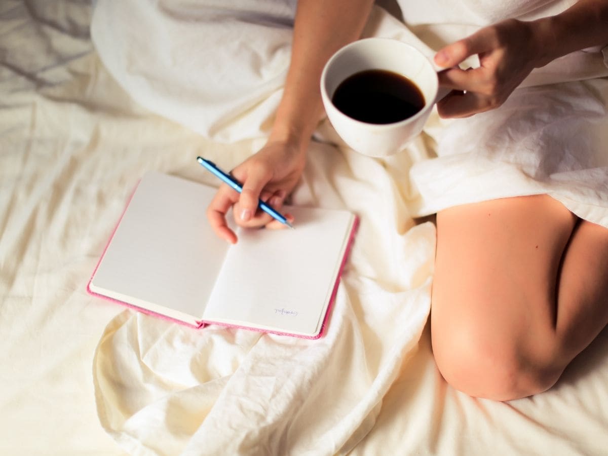 Female sitting in bed with coffee writing in gratitude journal.