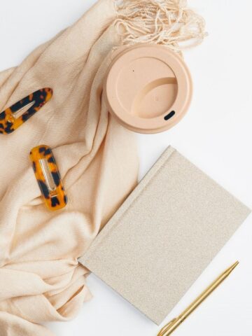 A pink scarf with barettes on top and a journal and pen nearby.