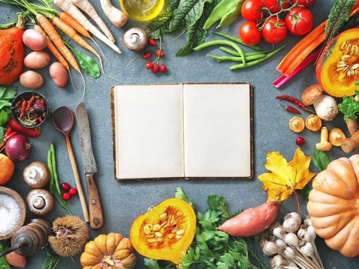 A notebook on a grey counter circled by fresh produce and spices.