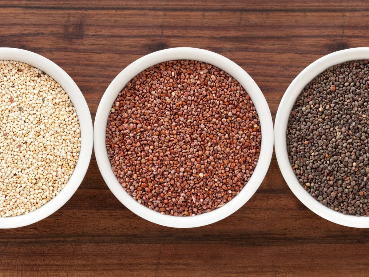 White, red and black quinoa in bowls on a wooden counter.