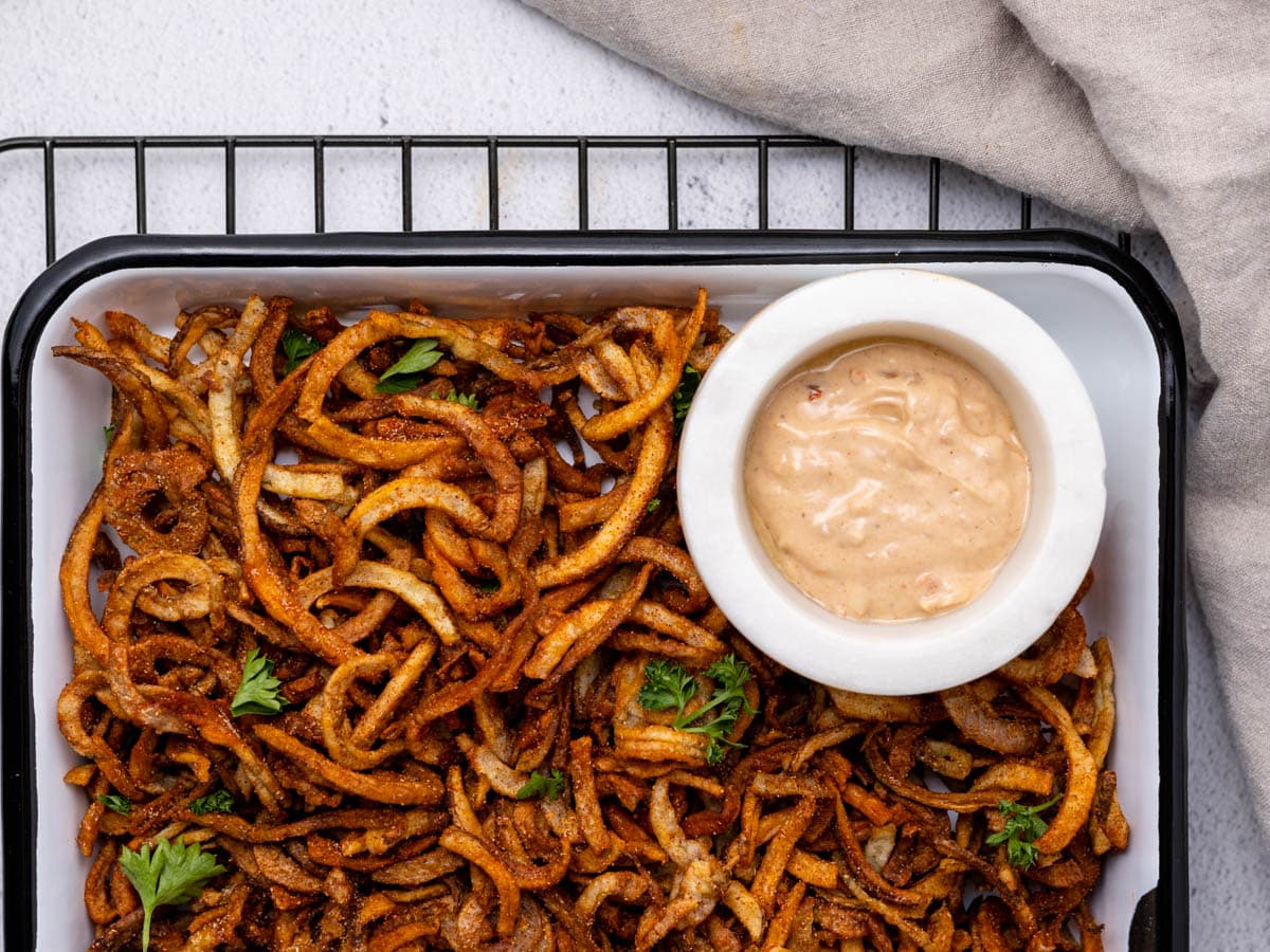 A tray of curly fries on a cooling rack with a spicy mayo dipping sauce.