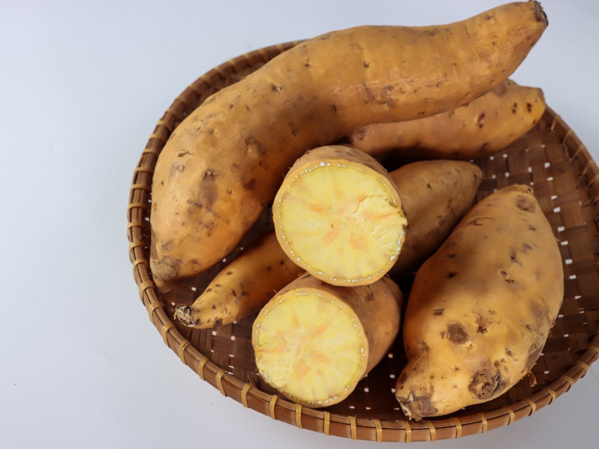 White sweet potatoes cut open in a wooden basket.