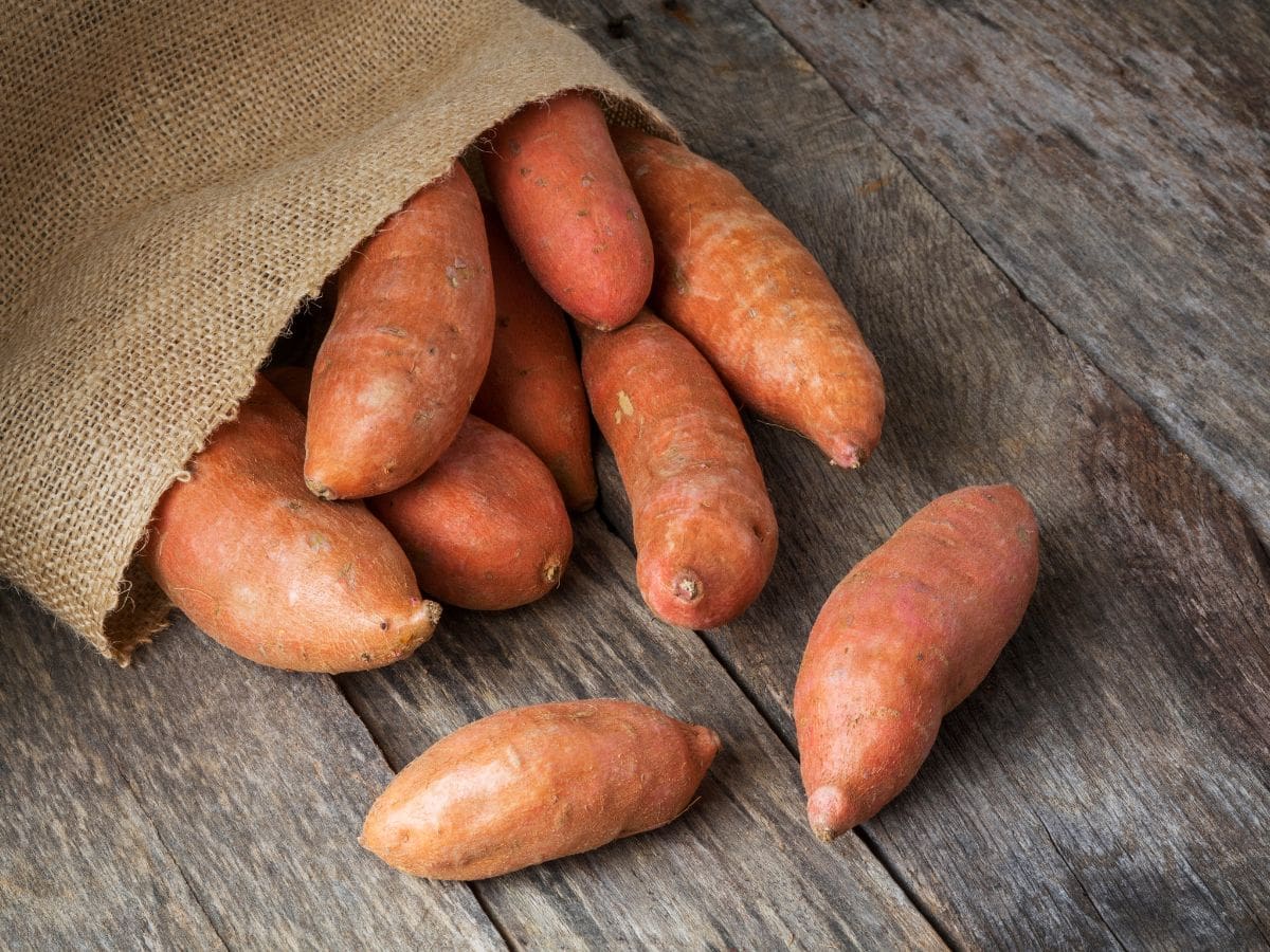 Sweet potatoes in a burlap sack on a wooden countertop.