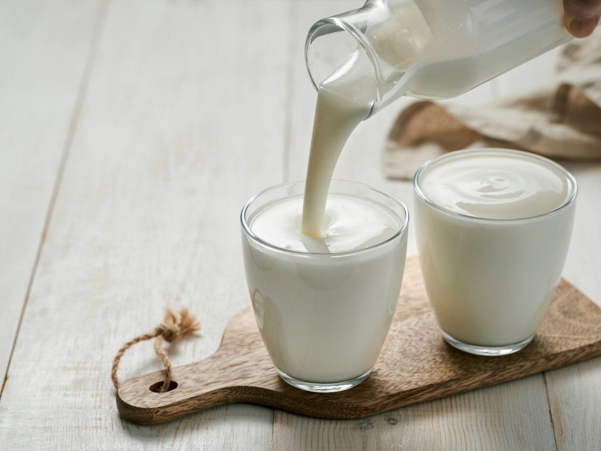 Kefir being poured into a glass sitting on a wooden cutting board.