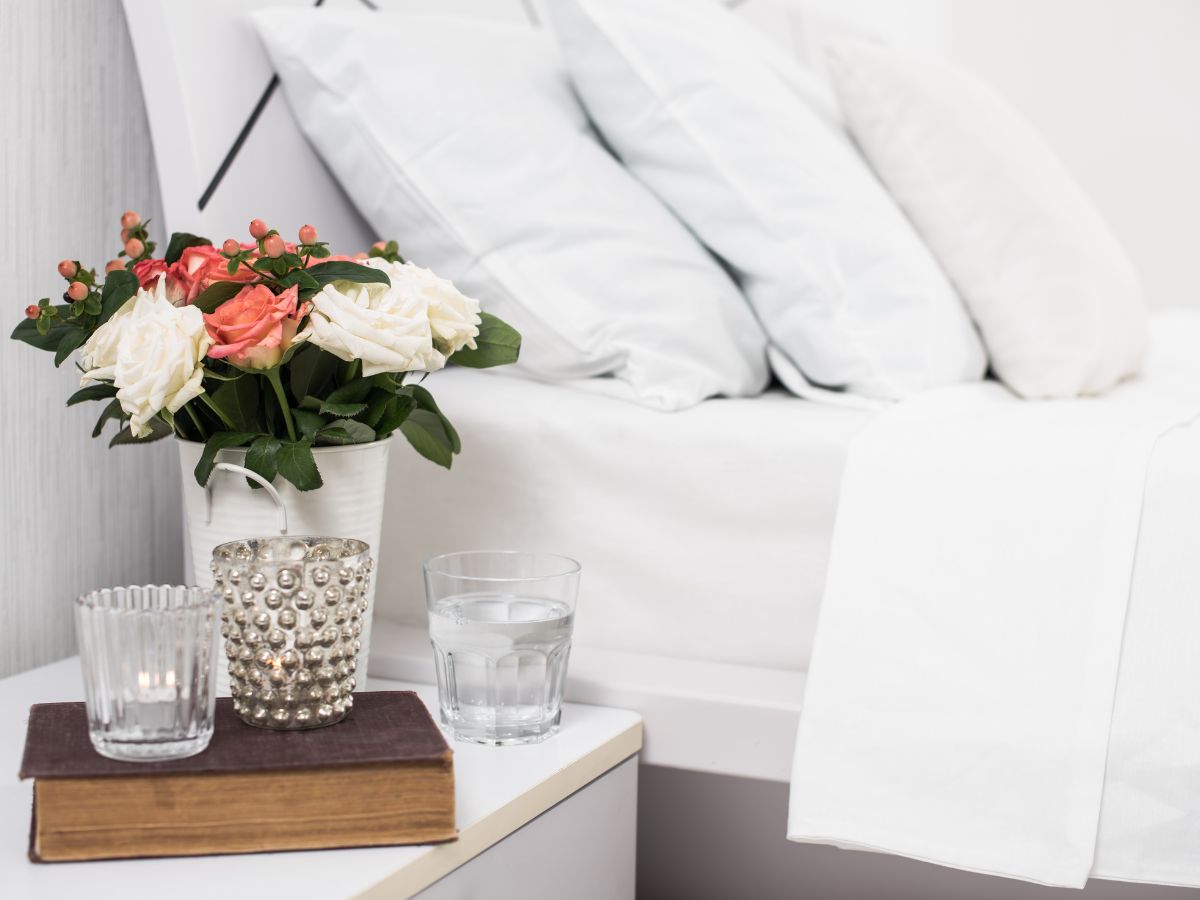 A white bed with flowers on the bedside table.