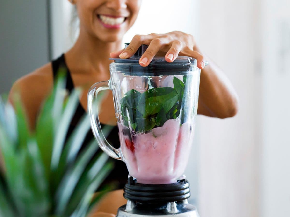 A girl making a smoothie with a green plant in front of it.