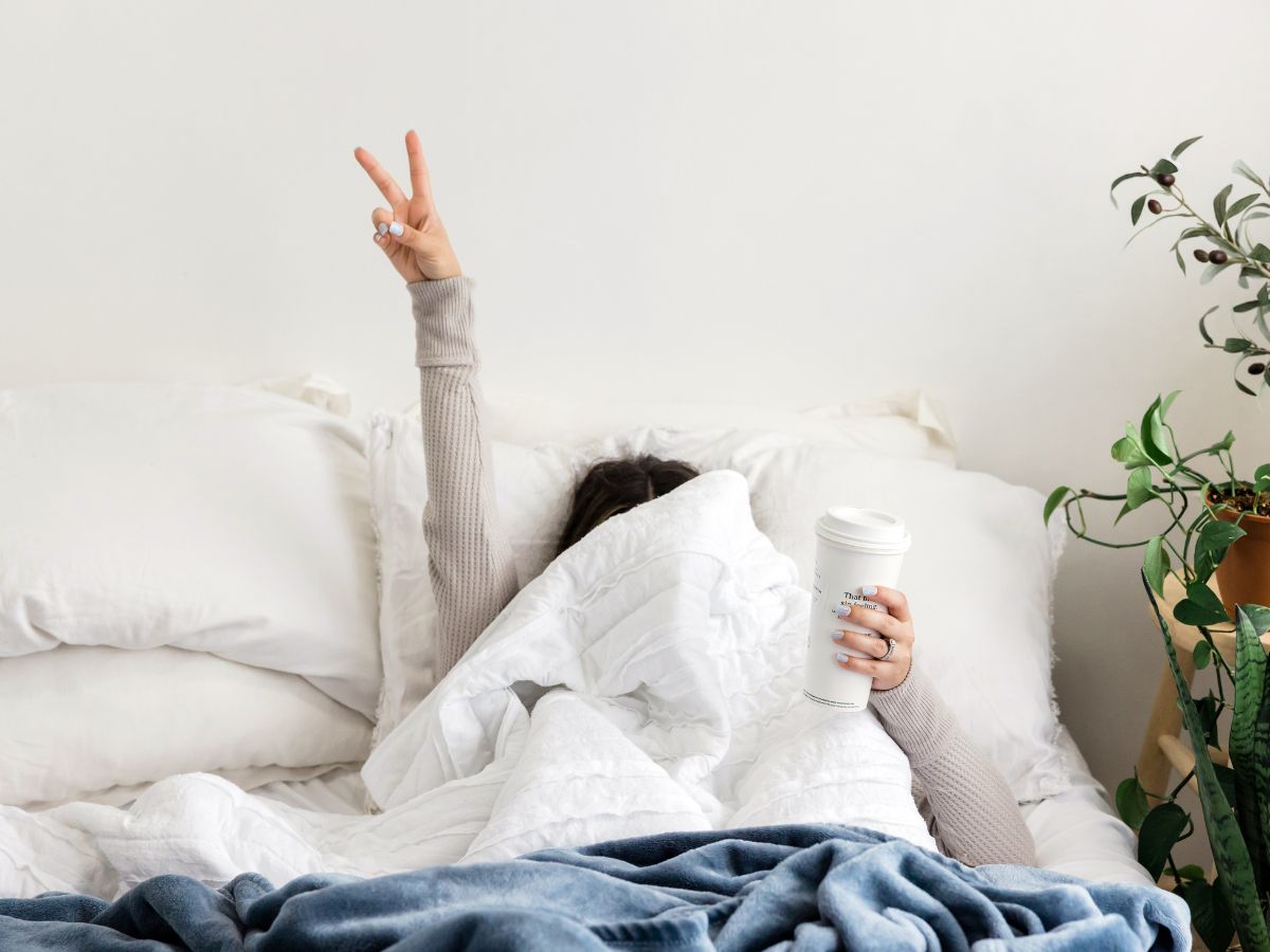 A girl in bed doing a peace sign.