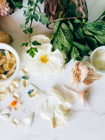 Herbal remedies and supplements on a white countertop with a white flower in the middle.