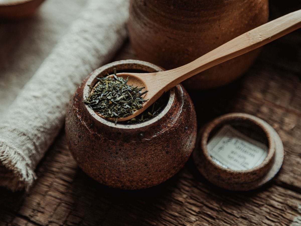 A wooden spoon filled with adaptogenic herbs resting a wooden pot.
