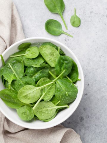A bowl of fresh spinach on a grey countertop.