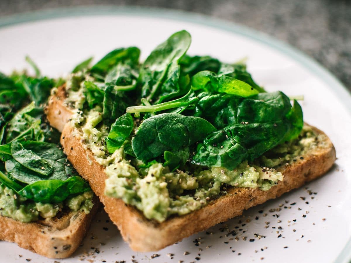 A piece of avocado toast with fresh spinach on top.