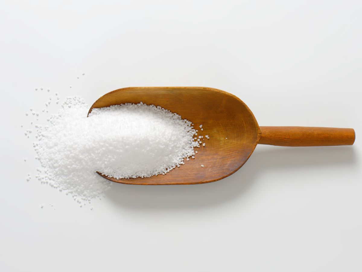 A wooden spoon with kosher salt in it on a white countertop.