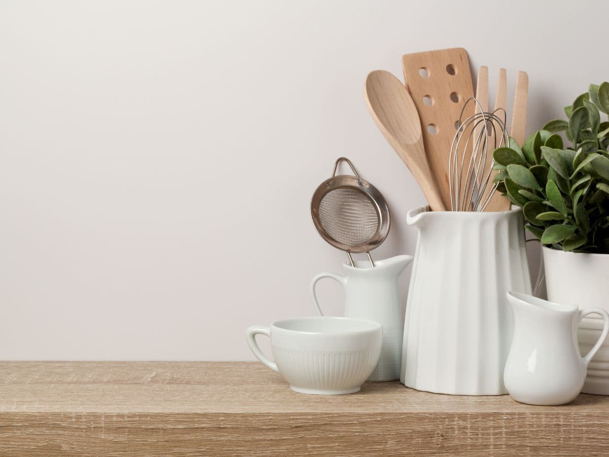 Wooden kitchen utensils in a white holder on a wooden countertop.