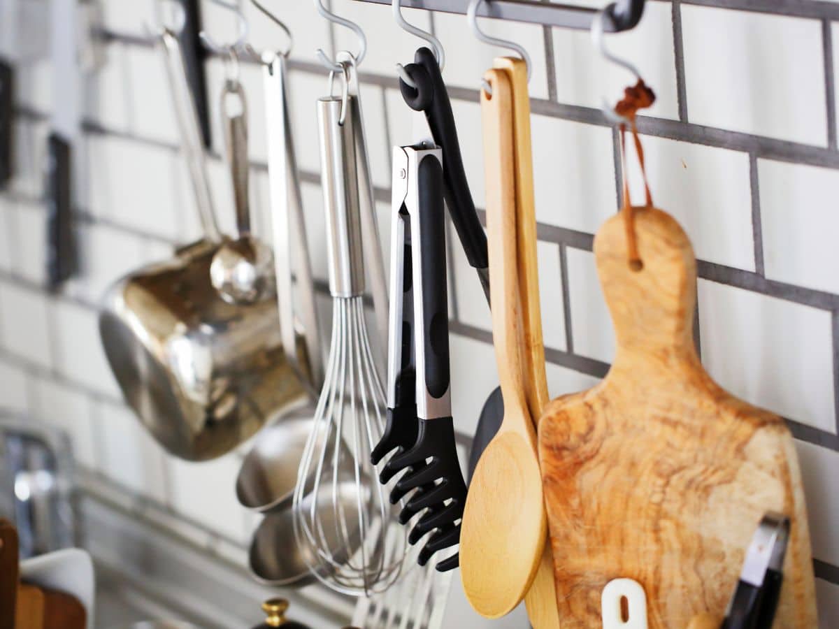 A variety of kitchen utensils hanging against a white tiled wall.