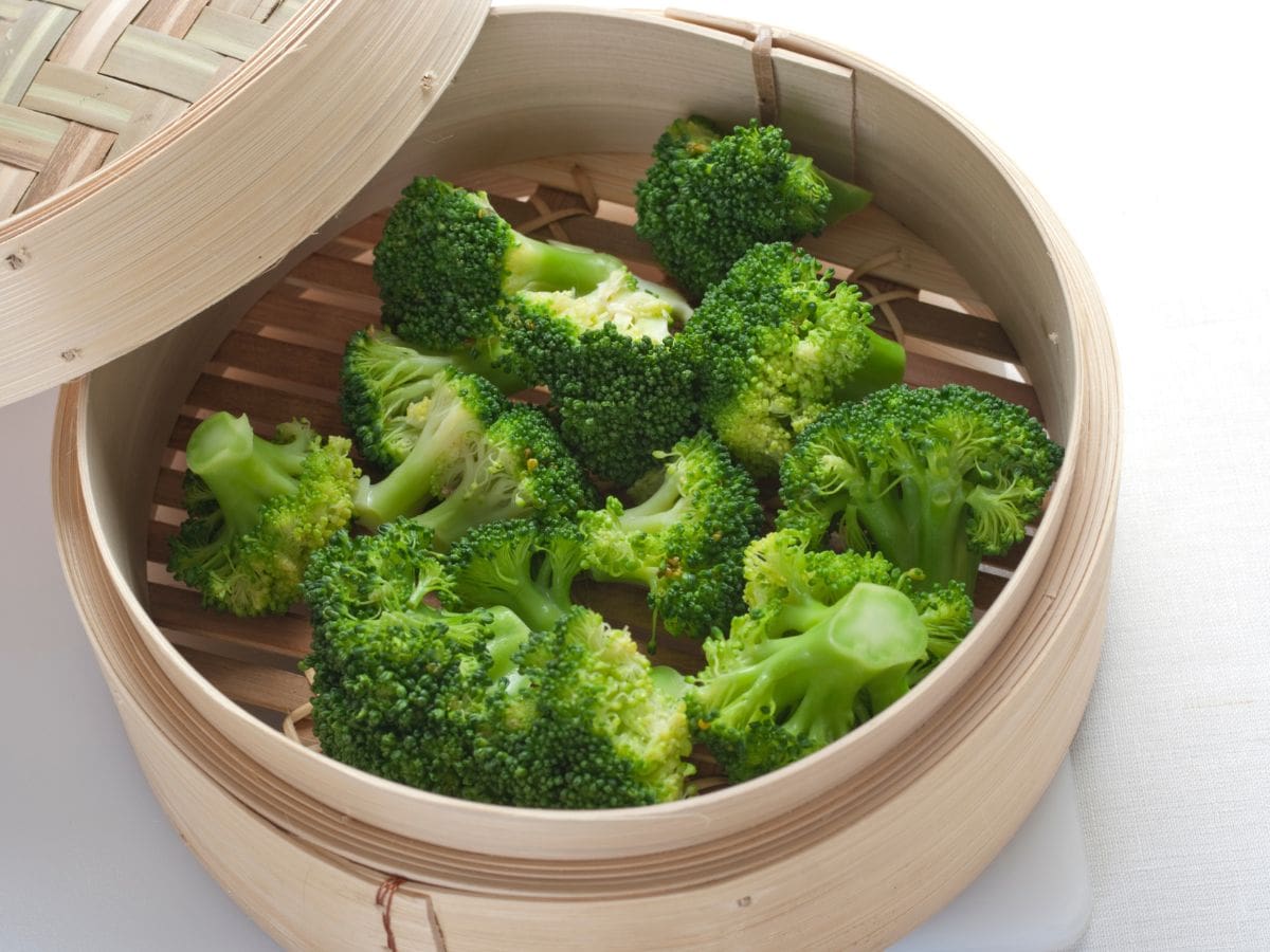 A bamboo steamer basket with broccoli in it.