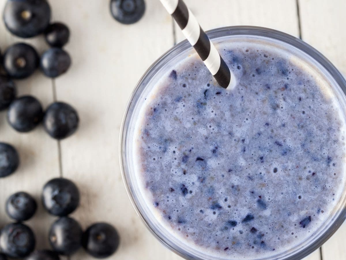 Overhead shot of blueberry smoothie on white countertop with blueberries alongside it.