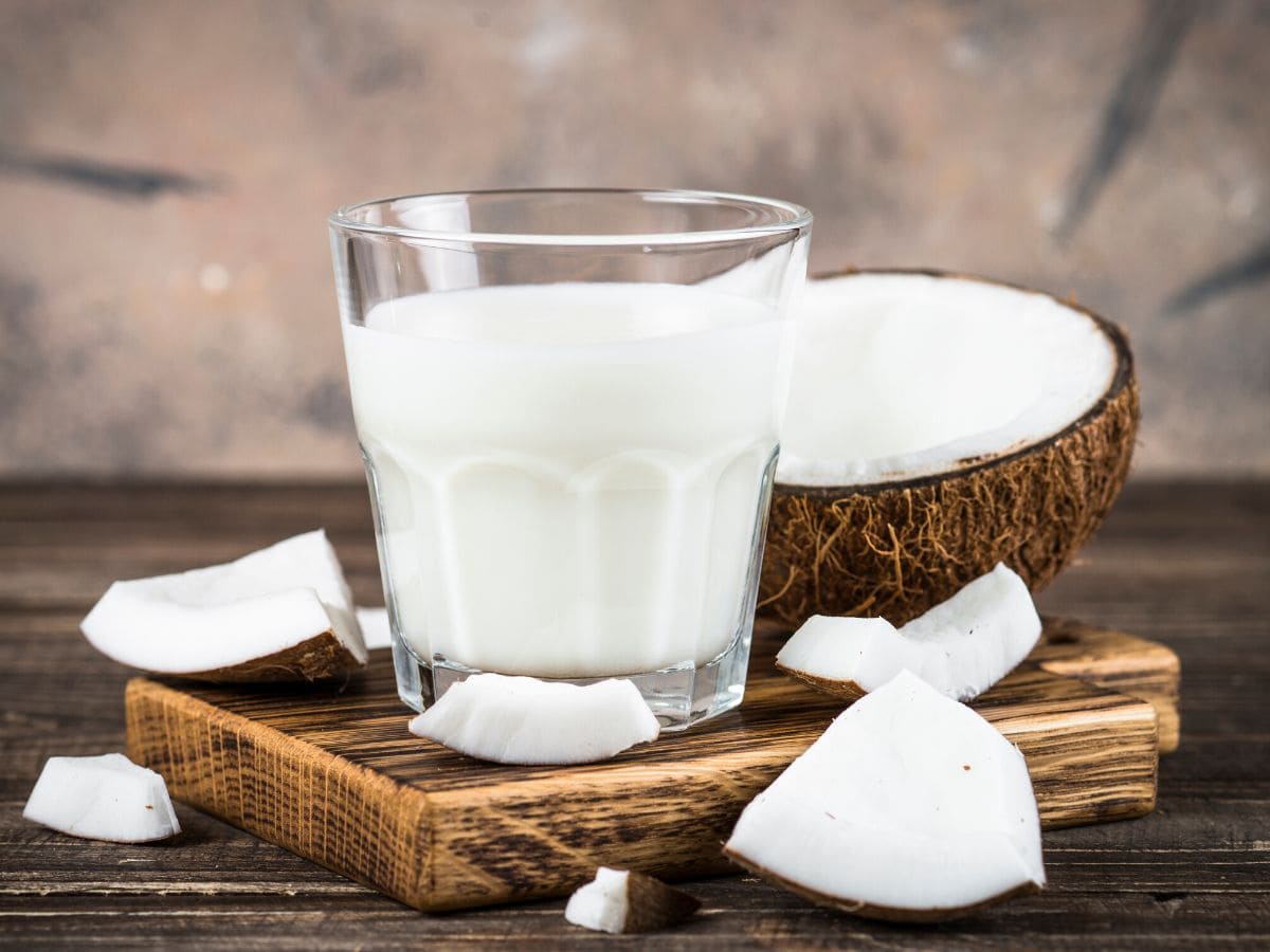 A glass of coconut milk with a cut open coconut behind it.