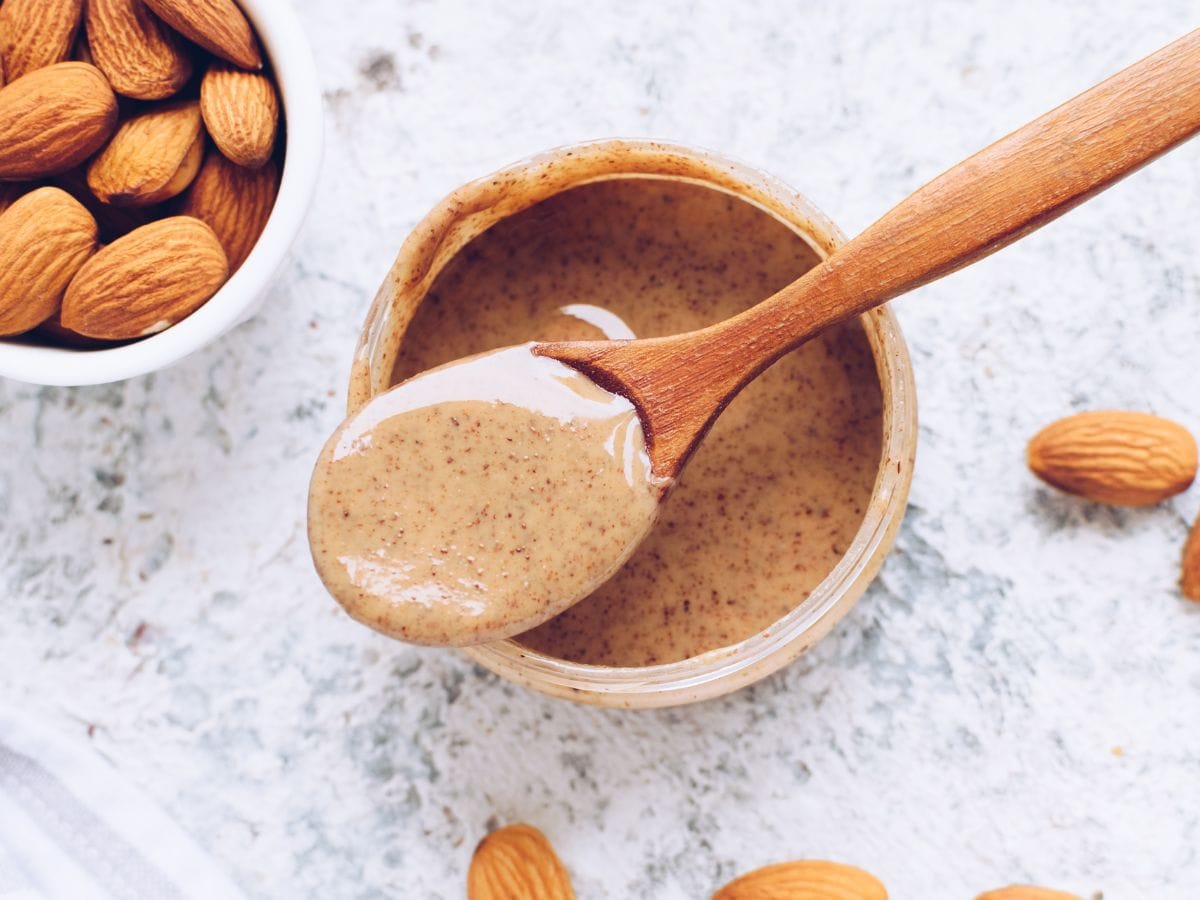 A spoonful of nut butter on top of a wooden bowl of nut butter.